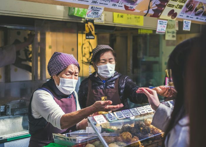 Two elderly Japanese ladies working at a food stall, reaching out to accept money.